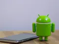 Zielony robot Android obok telefonu, symbolizujący najnowszą wersję systemu android 14.