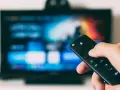Ręka trzymająca pilot do telewizora, gotowa do nauki, jak zainstalować aplikacje na telewizorze.