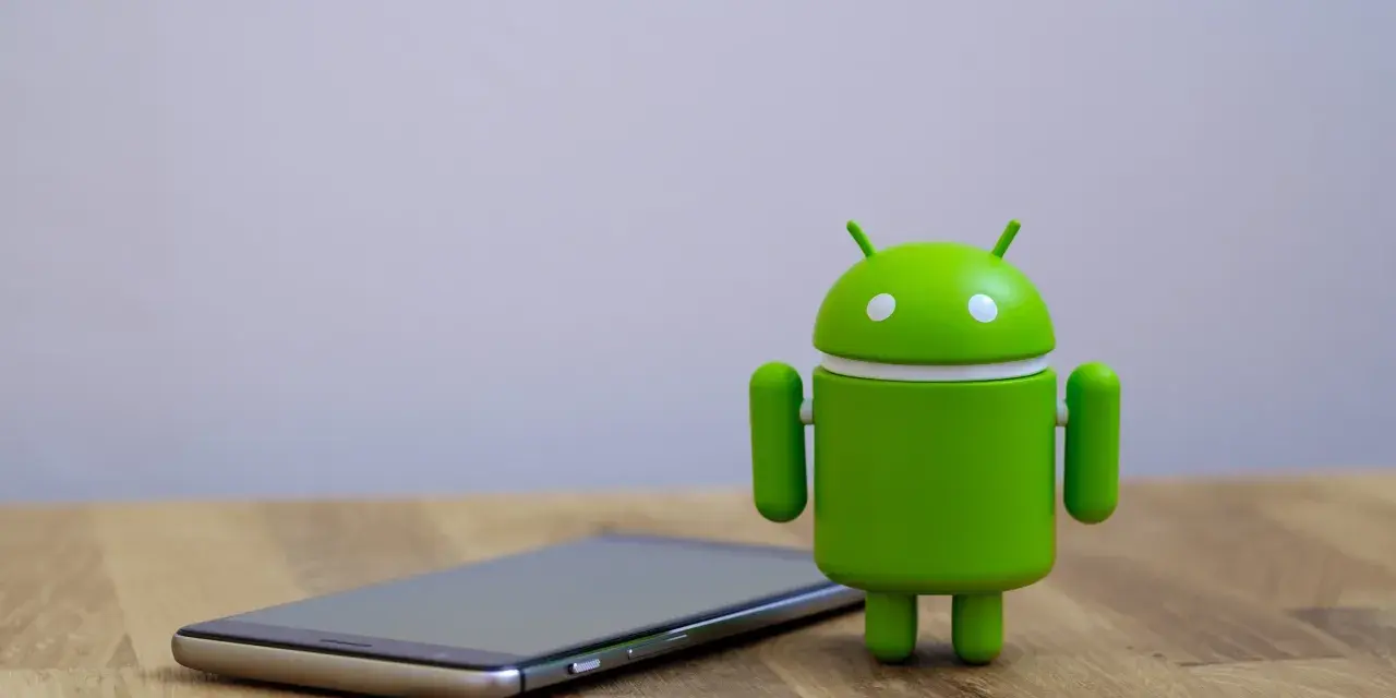 Zielony robot Android obok telefonu, symbolizujący najnowszą wersję systemu android 14.