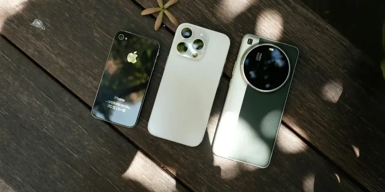 Trzy telefony na drewnianym stole: stary iPhone, biały iPhone i zielony telefon z najlepszym aparatem Leica.