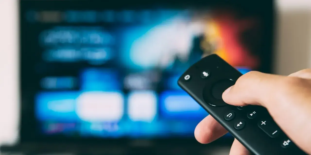 Ręka trzymająca pilot do telewizora, gotowa do nauki, jak zainstalować aplikacje na telewizorze.