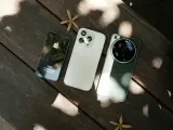 Trzy telefony na drewnianym stole: stary iPhone, biały iPhone i zielony telefon z najlepszym aparatem Leica.