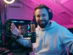 Uśmiechnięty streamer w słuchawkach, przed komputerem i mikrofonem, tłumaczy, streaming co to jest, w pokoju z różowym oświetleniem.