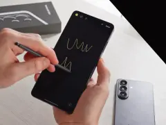 Ręce trzymają smartfon, rysując rysikiem na czarnym ekranie. Obok leży nowy Samsung S26, gotowy na premierę.