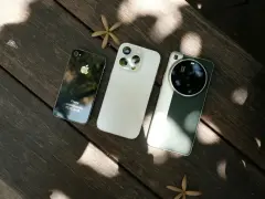 Trzy telefony na drewnianym stole: stary iPhone, biały iPhone i zielony telefon z najlepszym aparatem Leica.
