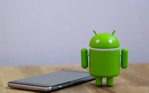 Zielony robot Android obok telefonu, symbolizujący najnowszą wersję systemu android 14.