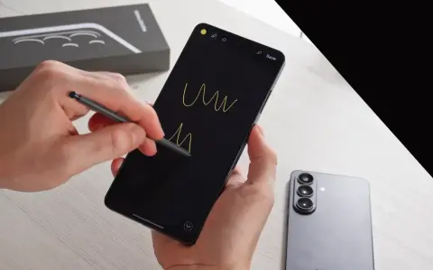 Ręce trzymają smartfon, rysując rysikiem na czarnym ekranie. Obok leży nowy Samsung S26, gotowy na premierę.