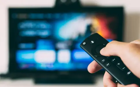Ręka trzymająca pilot do telewizora, gotowa do nauki, jak zainstalować aplikacje na telewizorze.