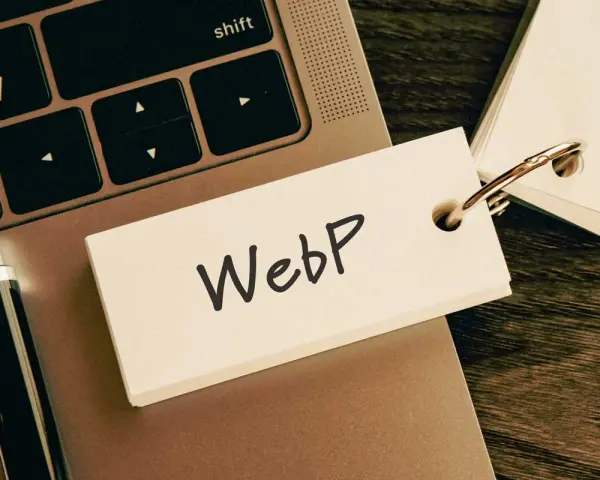 Notatka z napisem "WebP" na karcie przyczepionej do breloczka, leżąca na klawiaturze laptopa obok długopisu.