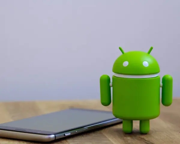 Zielony robot Android obok telefonu, symbolizujący najnowszą wersję systemu android 14.