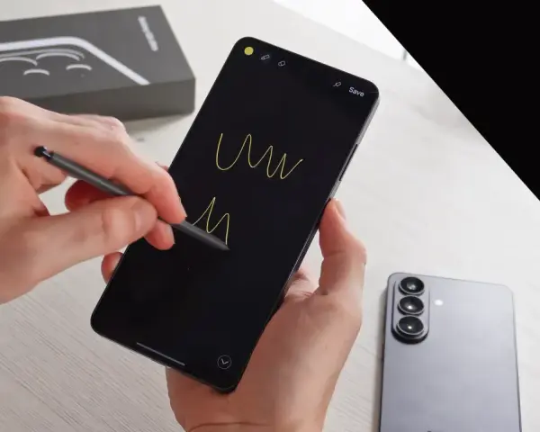 Ręce trzymają smartfon, rysując rysikiem na czarnym ekranie. Obok leży nowy Samsung S26, gotowy na premierę.