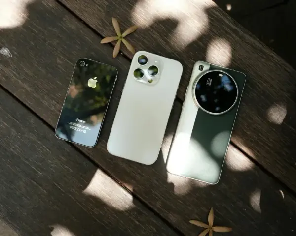 Trzy telefony na drewnianym stole: stary iPhone, biały iPhone i zielony telefon z najlepszym aparatem Leica.
