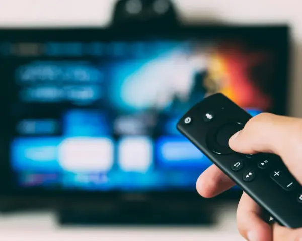 Ręka trzymająca pilot do telewizora, gotowa do nauki, jak zainstalować aplikacje na telewizorze.