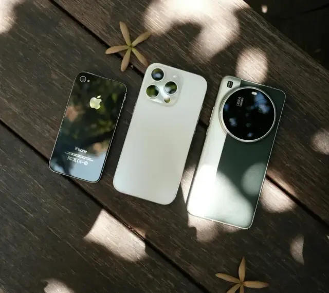 Trzy telefony na drewnianym stole: stary iPhone, biały iPhone i zielony telefon z najlepszym aparatem Leica.