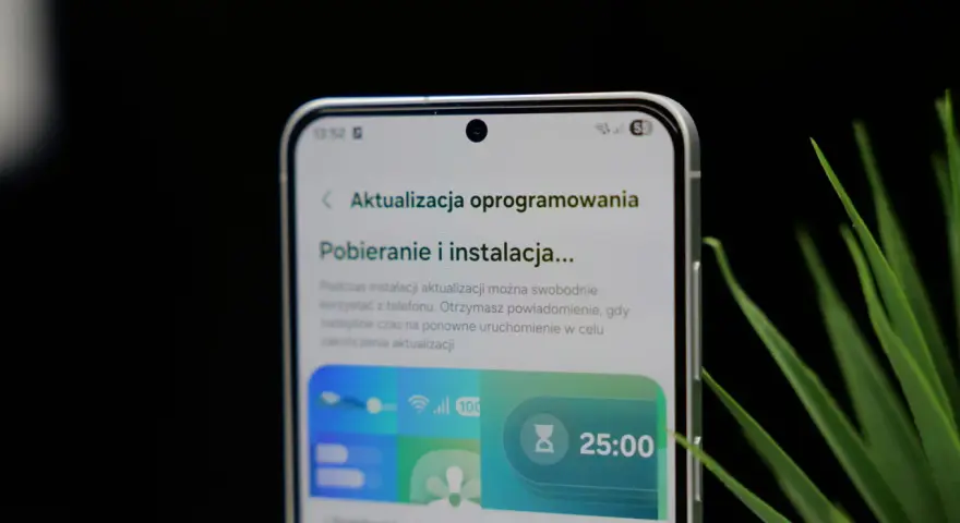 Telefon z interfejsem One UI 8.5 pokazuje ekran pobierania aktualizacji oprogramowania. Widoczny jest zegar 25:00.
