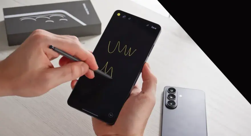 Ręce trzymają smartfon, rysując rysikiem na czarnym ekranie. Obok leży nowy Samsung S26, gotowy na premierę.