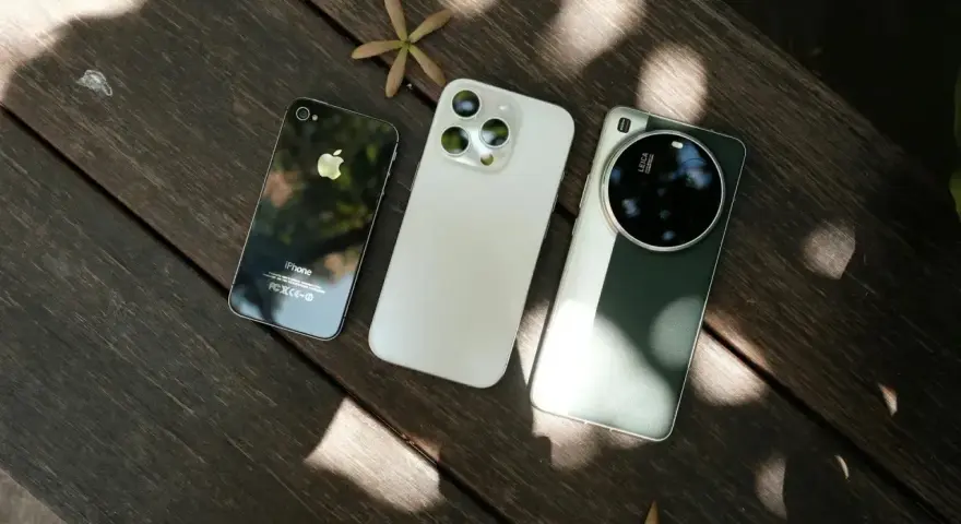 Trzy telefony na drewnianym stole: stary iPhone, biały iPhone i zielony telefon z najlepszym aparatem Leica.