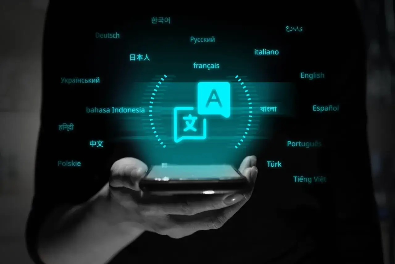 Dłoń trzyma smartfon z ikoną translatora. Wokół wyświetlają się nazwy języków: polski, angielski, francuski, niemiecki i inne.