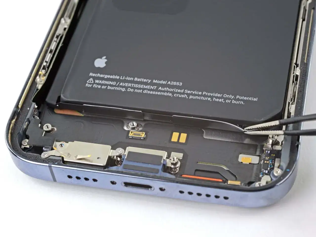 Precyzyjna wymiana baterii iPhone 14 Pro. Pęseta delikatnie podważa taśmę baterii, rozpoczynając proces serwisowy.