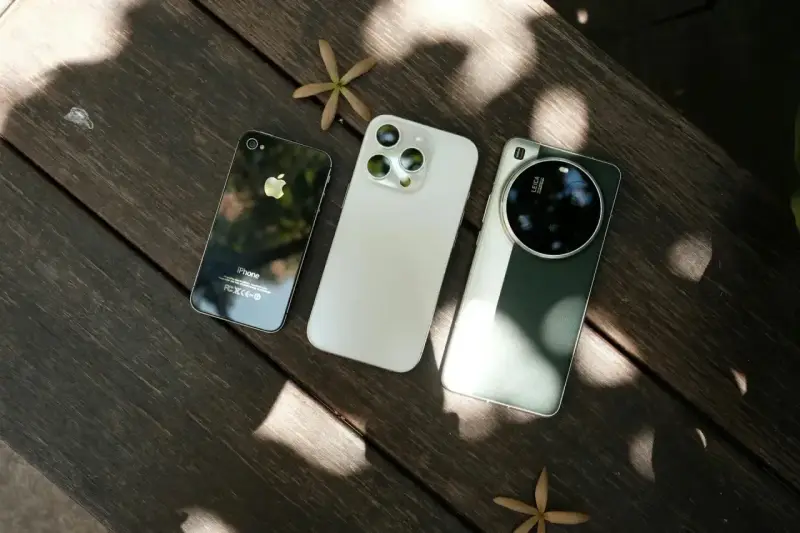 Trzy telefony na drewnianym stole: stary iPhone, biały iPhone i zielony telefon z najlepszym aparatem Leica.